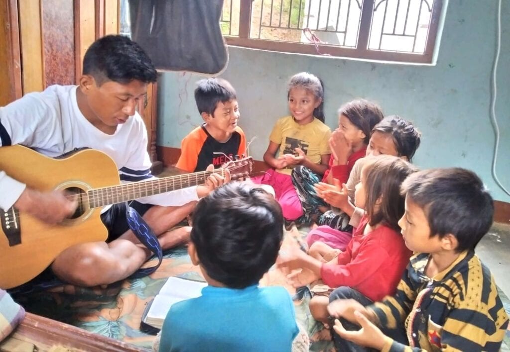 Mladý muž hraje na kytaru skupince dětí.